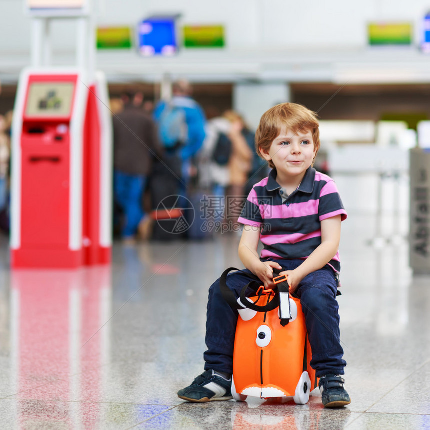 美丽的金发男孩在机场的室内享受自家行李图片