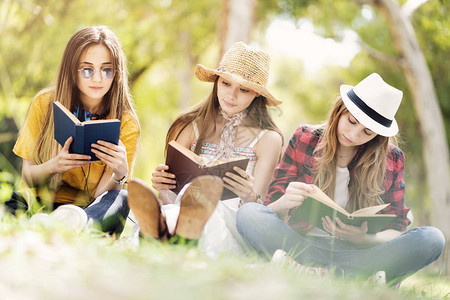 年轻的朋友们坐在外面的草地上看书背景图片