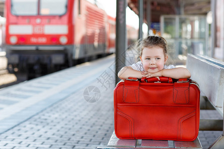 在火车站拿着大红色手提箱的可爱小女孩图片