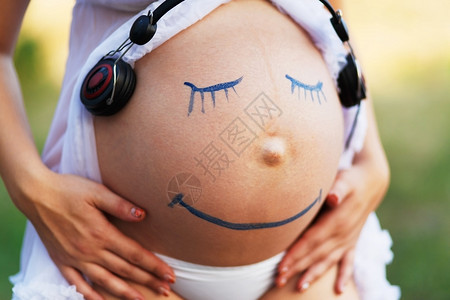 胎教孕妇腹部特写与笑脸画在户外听音乐在女人肚子上的耳机怀孕快乐背景图片
