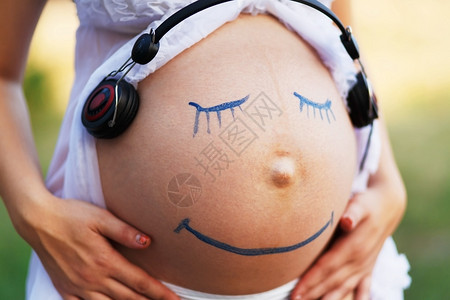 胎教孕妇腹部特写与笑脸画在户外听音乐在女人肚子上的耳机怀孕快乐背景图片