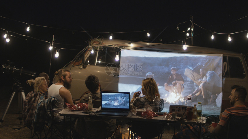 一群朋友在晚上看面包车屏幕上的电影时图片