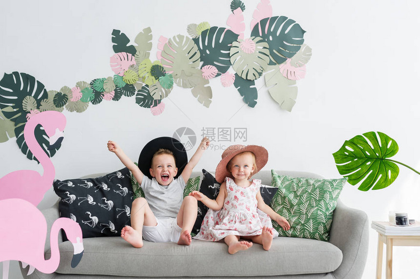快乐微笑的男孩和女孩戴着草帽在房间的沙发上玩耍蹒跚学步的图片