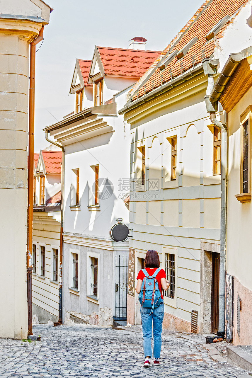 一名携带背包的女游客在欧洲一个无法辨认的城市的浪漫和狭窄的街道上旅图片