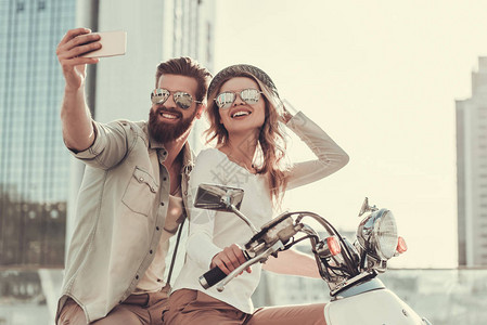 戴太阳眼镜的年轻美女夫妇正在使用智能手机进行自拍图片