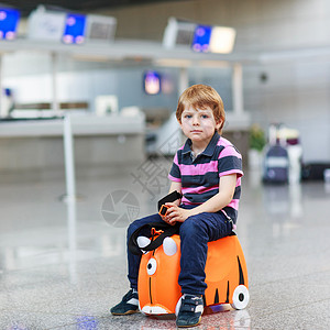美丽的金发男孩在机场室内有好玩的手提箱图片