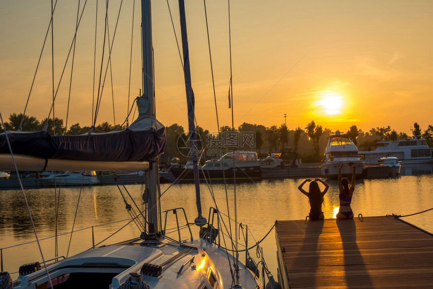 在游艇俱乐部的美丽日落在泊位的帆船在夕阳的背景下的游艇女孩们图片