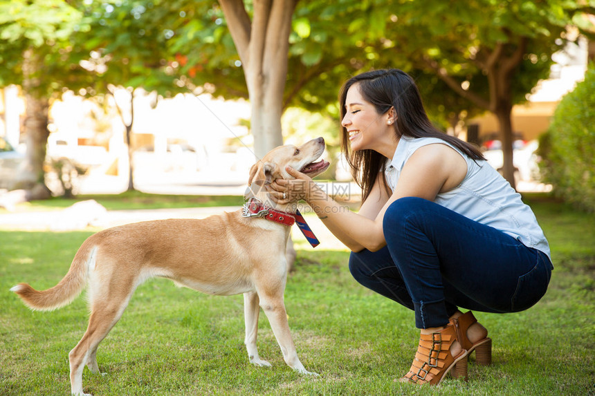 一位美丽的年轻女子在公园里抚摸她的狗并亲吻图片
