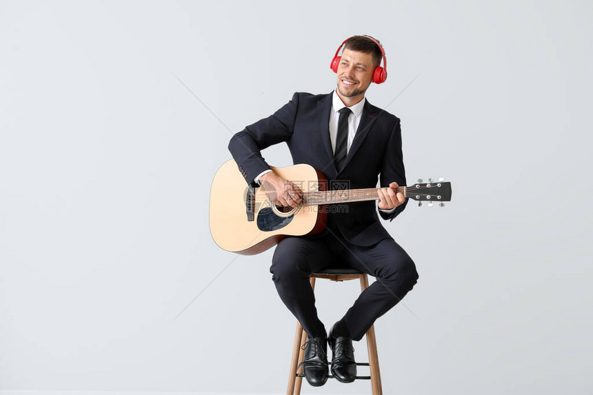 英俊的男人在浅色背景下弹吉他图片