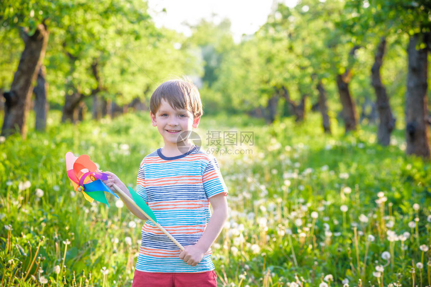 一个快乐可爱的小男孩在公园里拿着风车的画像孩子牵手玩风车男孩在春天或夏天的森林里微笑户外休闲图片