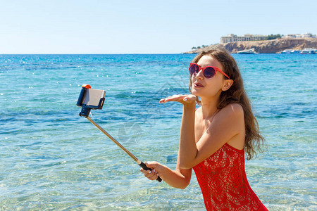 穿泳衣的女孩在沙滩上用智能手机在图片