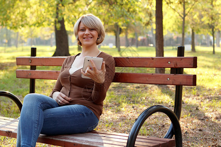 美丽的女人坐在公园里玩平板电脑图片
