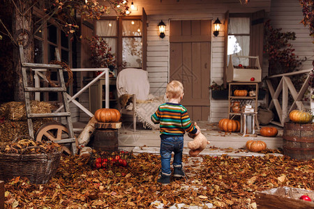 可爱的小男孩穿着毛衣牛仔裤蓝色靴子在房子附近玩毛绒玩具泰迪熊图片