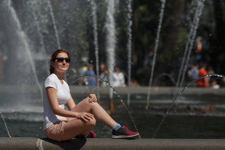 美丽的女人坐在喷泉背景的太阳镜里图片