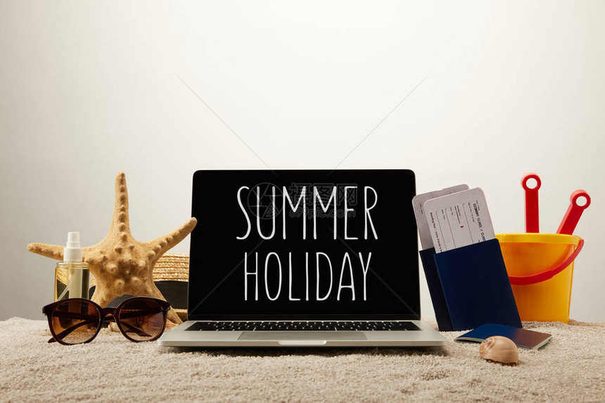 带暑假字样海星太阳镜带门票的护照和灰色背景沙子上的玩具桶的笔记本电图片