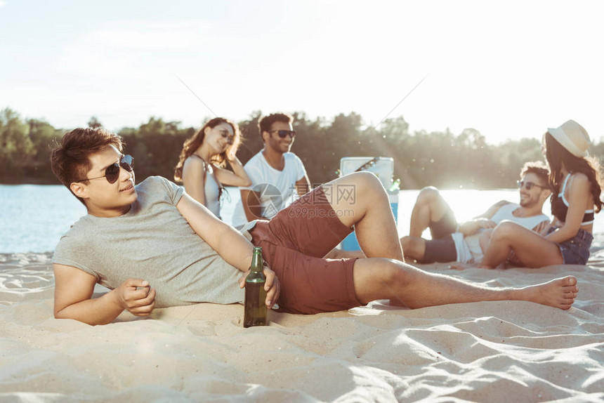 年轻男子躺在沙滩上而她的朋友图片