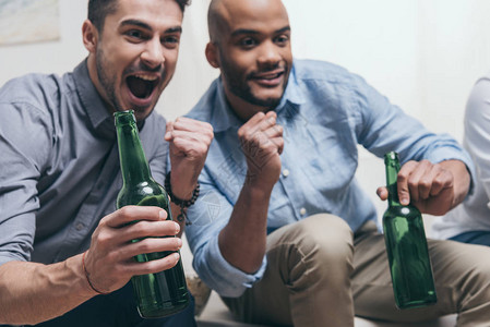 多民族男子在家看足球和喝啤酒时观图片
