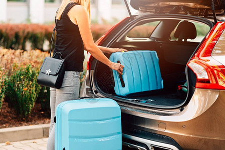 妇女将两个蓝色塑料手提箱装上汽车后备箱图片