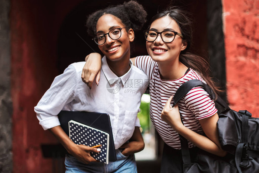 两个漂亮的笑脸女孩戴着笔记本和背包的眼镜快乐地在户图片