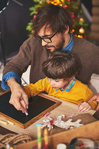 年幼的父亲教儿子在圣诞节的时候用粉笔和图片