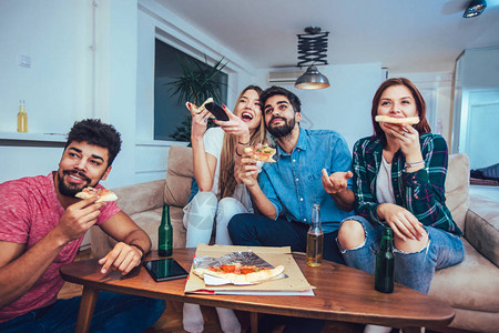 一群年轻朋友在家里吃披萨喝啤酒和看电视图片