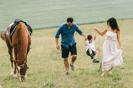 父母亲和儿子手牵田野上在马匹图片