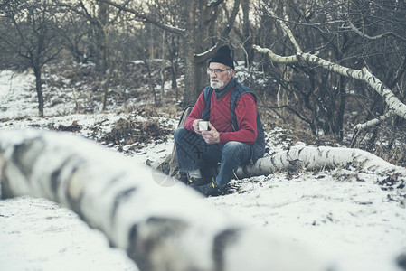 孤独的老人坐在雪地里倒下的树干上图片