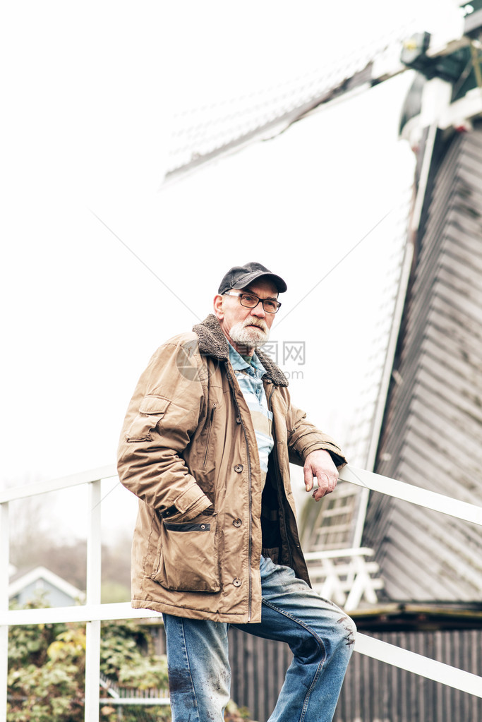 在冬季风景中长胡子戴眼镜和黑帽的老人身处户外图片