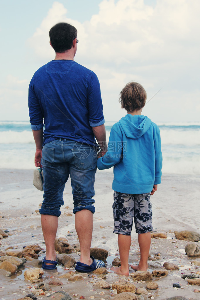 父亲和儿子在海滩上走着看着晚上的距图片