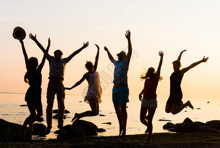 快乐的朋友们享受日落和在海滨上跳跃青年假期海滩派图片