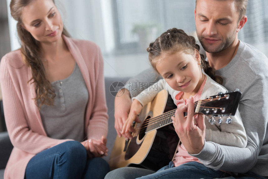 父亲教女儿如何弹声吉他而母亲却坐在沙发上图片