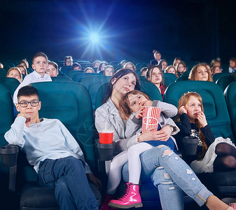 漂亮的师姐带着小孩子在新的电影院看电影或卡通片孩子们看起来非常感兴趣并退出了背景背景