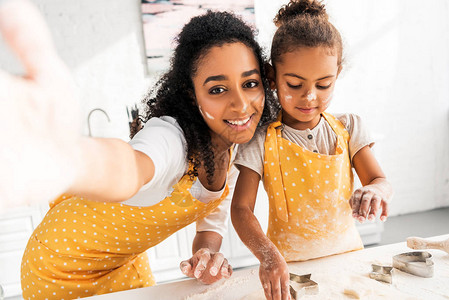 笑的美裔母亲和女儿在厨房用模具做饼干时图片