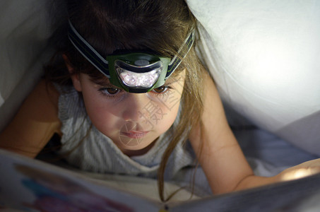 小孩56岁的女孩晚上在床底下的封面下阅读书FrontView图片