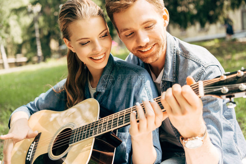 近距离拍摄的年轻微笑着的女士学习弹吉他在公园和男朋图片