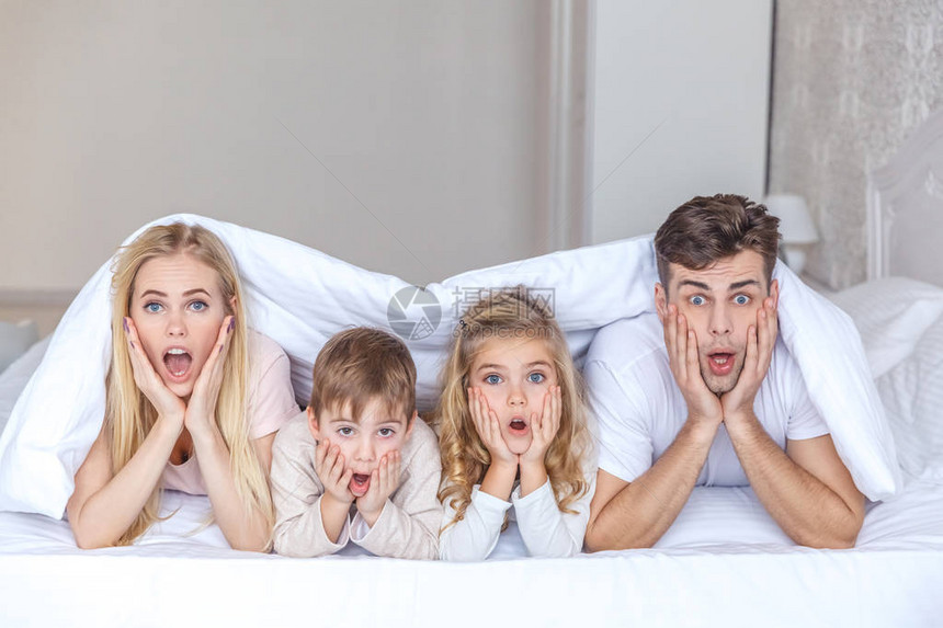 惊吓的年轻家庭躺在床上被毯子缠在床上图片