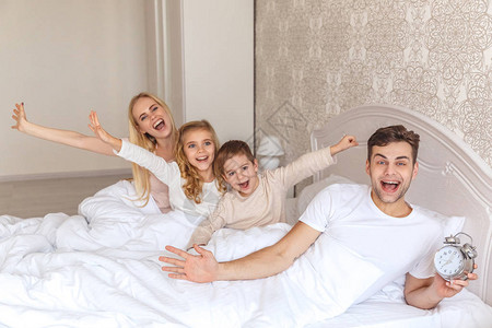 与闹钟一起醒来的快乐年轻家庭图片