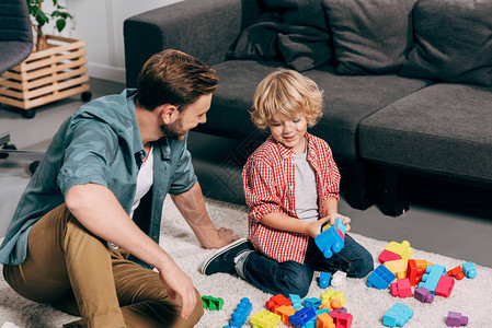 快乐的孩子和他父亲在家中的地板上玩着多彩塑料块游戏图片
