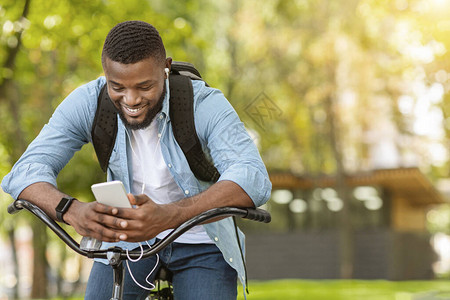 户外微笑的年轻非洲男子在街上拿着手机骑自行车下载音乐播放列表骑车上图片