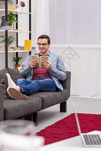 微笑的成年男子在家沙发上看书图片