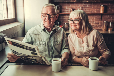 美丽的老夫妇在喝茶阅读报纸和在厨房休息图片