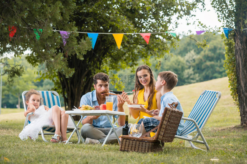 有两个孩子的专心致志的年轻父母在暑日家庭野餐期间一起吃饭时图片