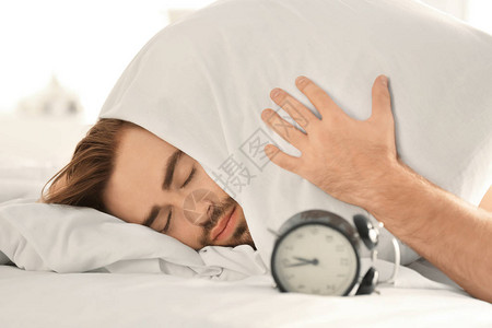 警钟和年轻人在睡觉时用枕头盖住头同时背景图片