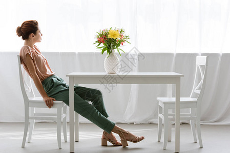 坐在桌边的有吸引力的年轻女子的一面家里独自用花瓶装图片