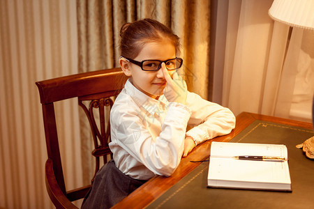 戴着笔记本和灯光坐在桌子后面的眼镜上的图片
