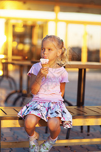 美丽的小女孩坐在长椅上吃着图片