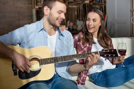 快乐的一对年轻夫妇一起在沙发上用吉他图片