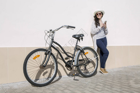 穿着帽子和太阳镜的笑脸女青年骑着自行车和工具站在墙边西班牙大加那利图片
