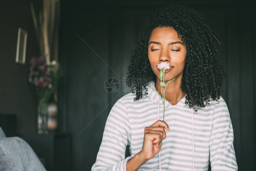 一个漂亮的黑女人的近身卷发头闻着一朵玫瑰花的香图片