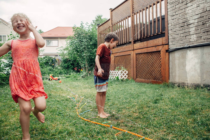 孩子们的朋友男孩女在夏日的后院用园艺软管洒水器泼水孩子们在家院子外面玩水有趣的家庭活动的坦率真实的图片